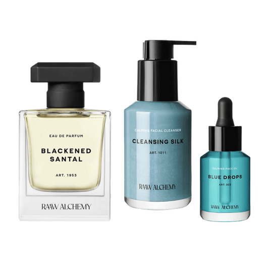 RAAW Alchemy Award Winning Bundle featuring Blackened Santal Eau de Parfum, Cleansing Silk facial cleanser, and Blue Drops facial oil on a transparent background.