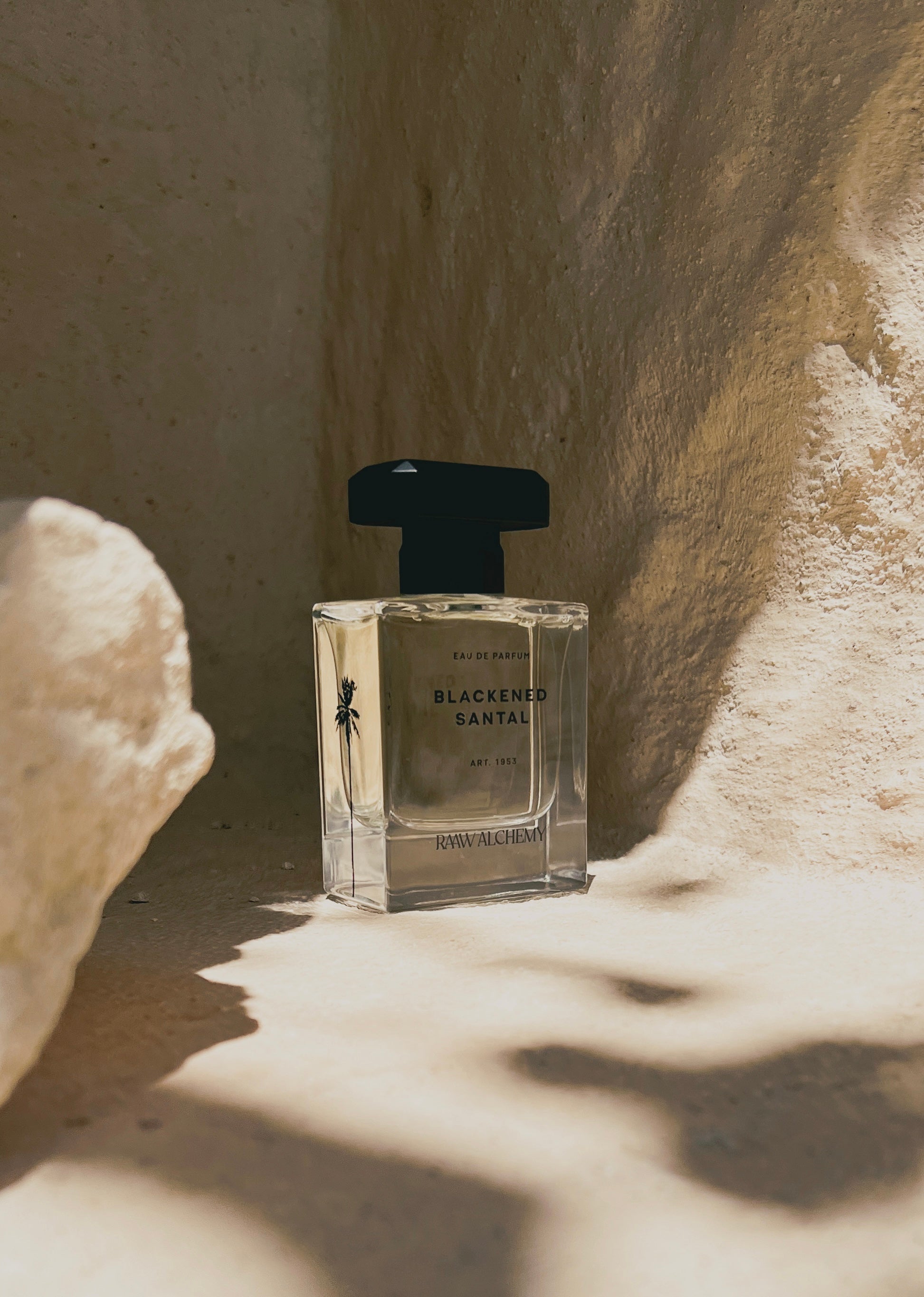 Blackened Santal Eau de Parfum bottle standing alone on a sun-drenched stone floor, creating soft shadows.
