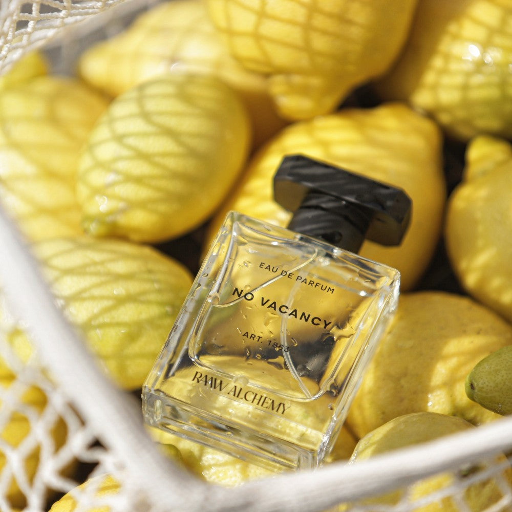 No Vacancy perfume bottle nestled in a net bag filled with fresh lemons, highlighting its citrus inspiration.
